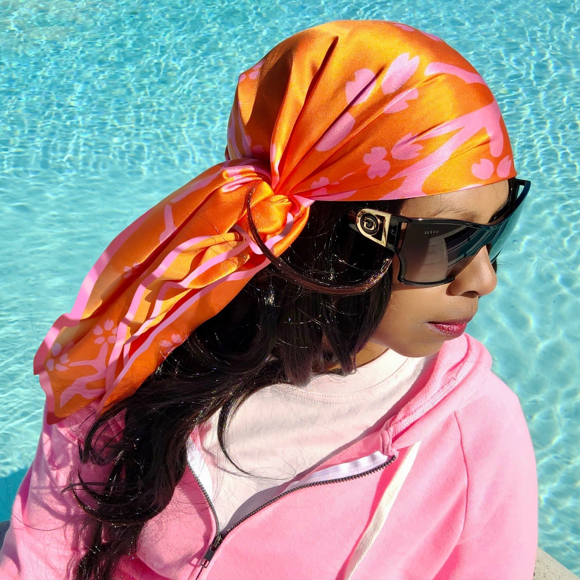 A woman wearing a Caribbaby pink and peach silk scarf around her head, at a pool