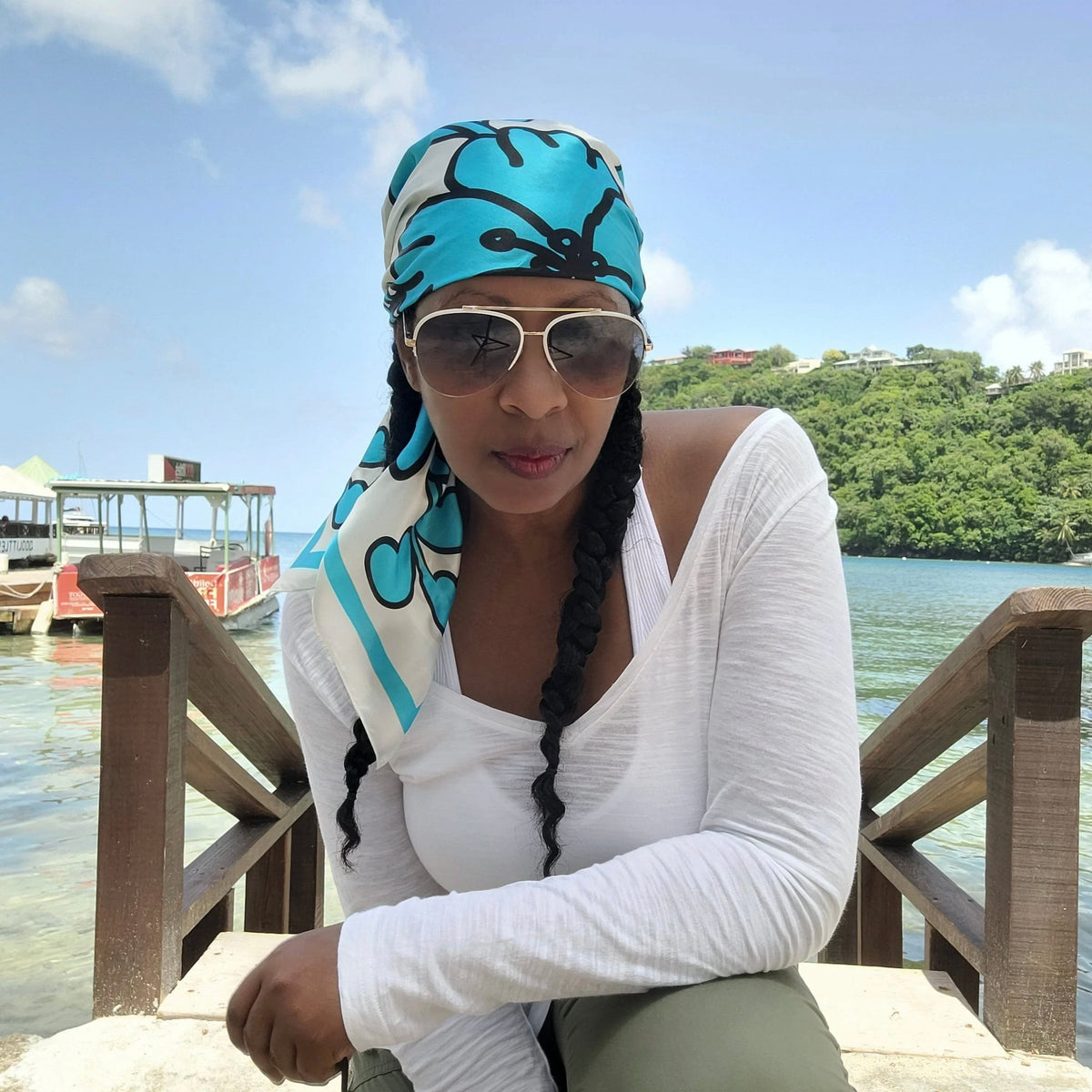 A woman wearing a Caribbaby silk scarf wrapped around her head, sitting on a tropical island.