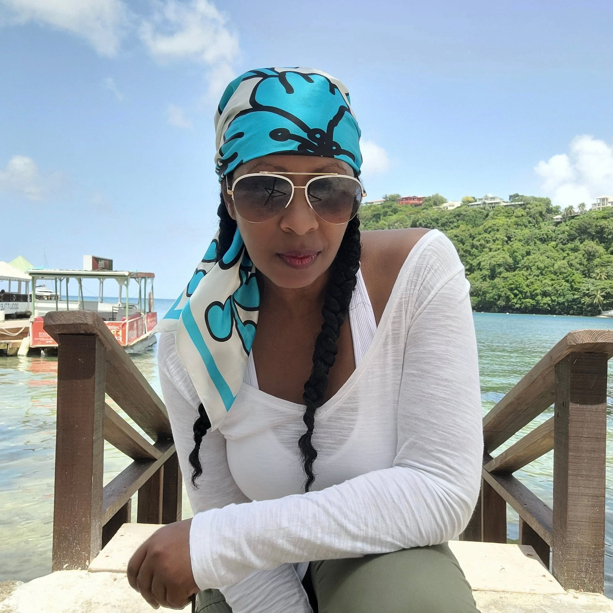 A woman wearing a Caribbaby silk scarf wrapped around her head, sitting on a tropical island.