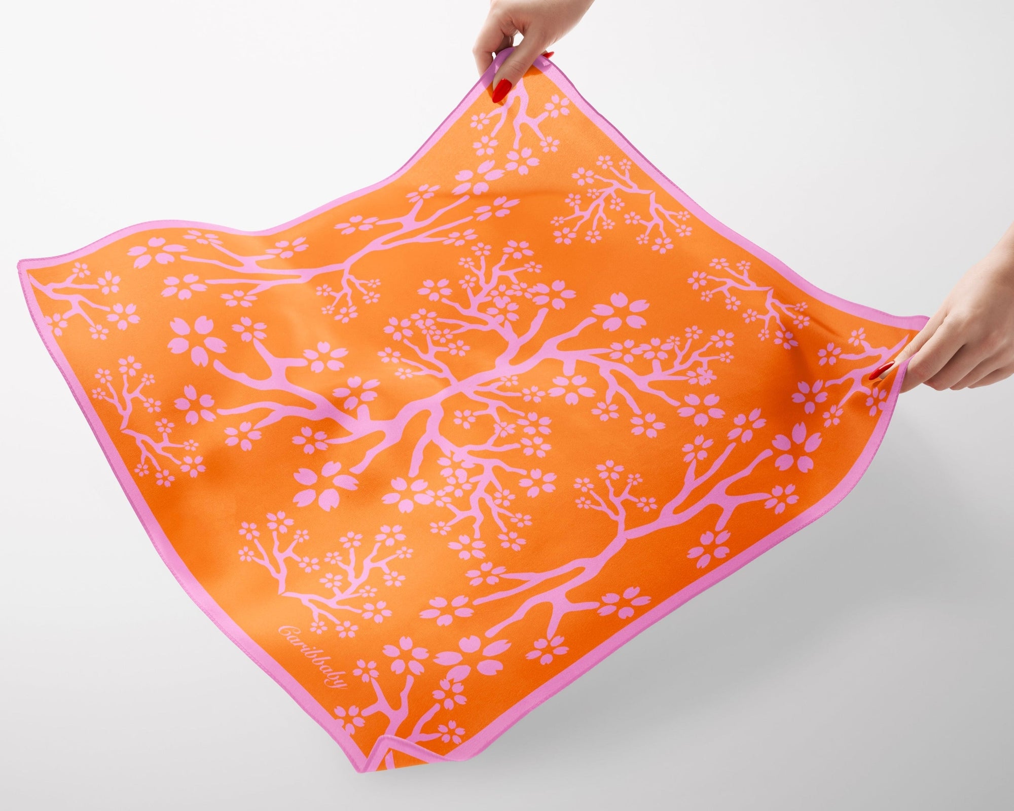 A pink and peach silk scarf being held by hands on a white background