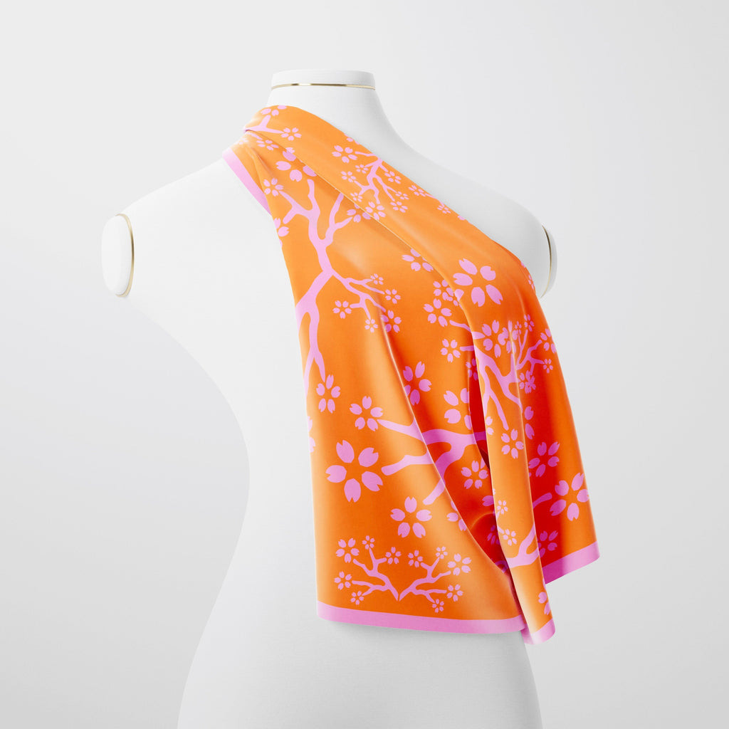 A pink and peach silk scarf drapped over a mannequin on a white background