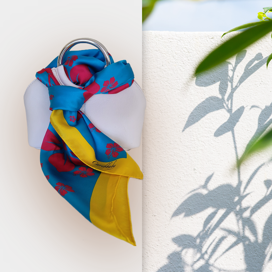 Silk scarf with Hibiscus pattern draped over a purse on a leafy background